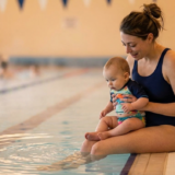 Mother introducing her baby to water during a newborn swimming lesson in an indoor pool