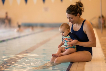 Mother introducing her baby to water during a newborn swimming lesson in an indoor pool